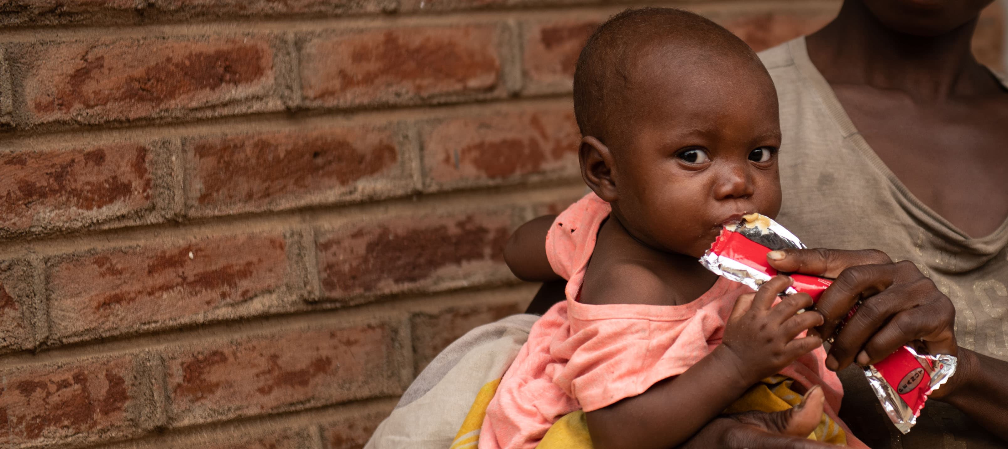 Barn med nötkräm / RUTF - i mammas famn - Malawi 2024 - cropped desktop